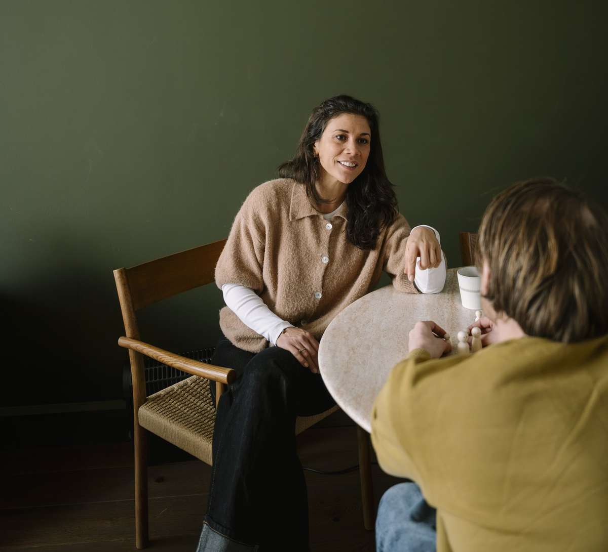 Iris in gesprek met een cliënt aan tafel voor een donkergroene muur