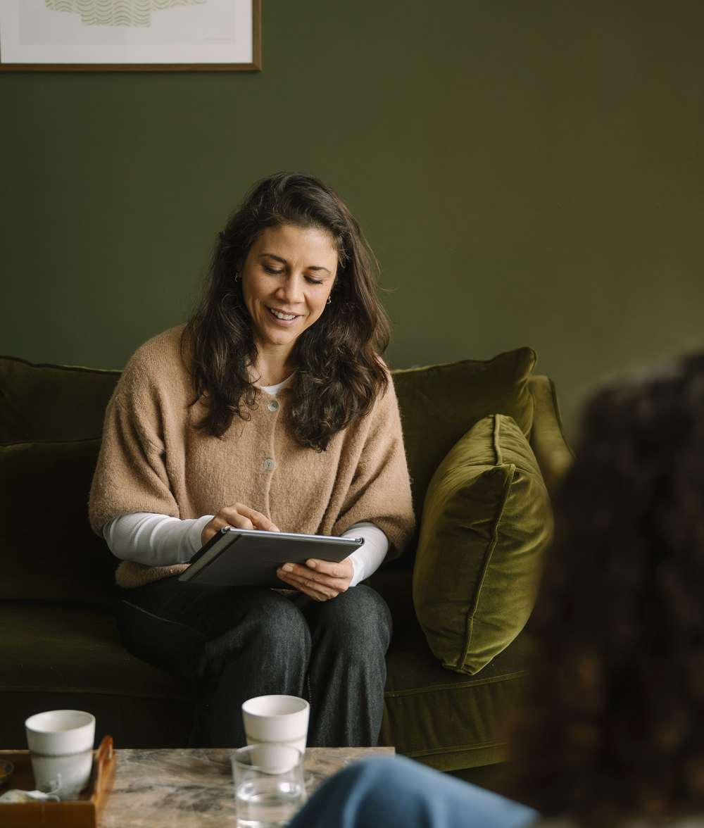 Iris op de groene bank met een tablet, in gesprek met een stel
